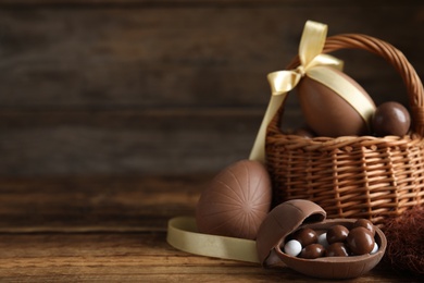 Photo of Composition with tasty chocolate eggs and wicker basket on wooden table, space for text