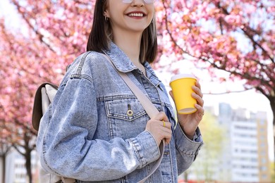 Young woman with paper cup near blossoming sakura tree in park, closeup