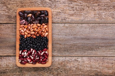 Plate with different kinds of dry kidney beans on wooden table, top view. Space for text