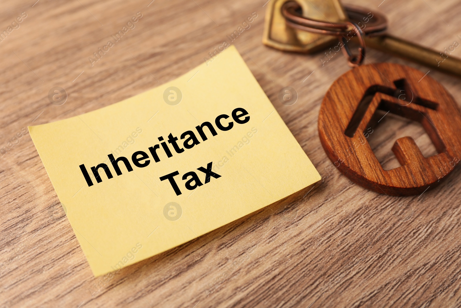 Photo of Inheritance Tax. Paper note and key with key chain in shape of house on wooden table, closeup