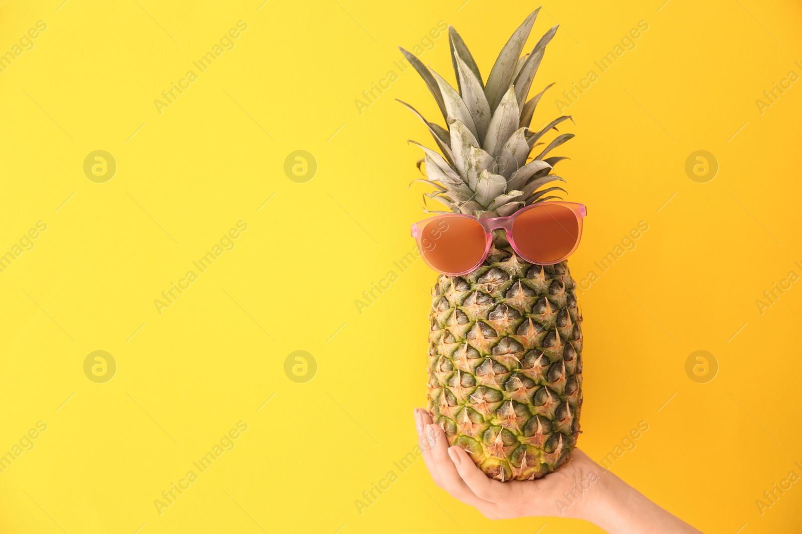 Photo of Woman holding fresh ripe pineapple with sunglasses on color background