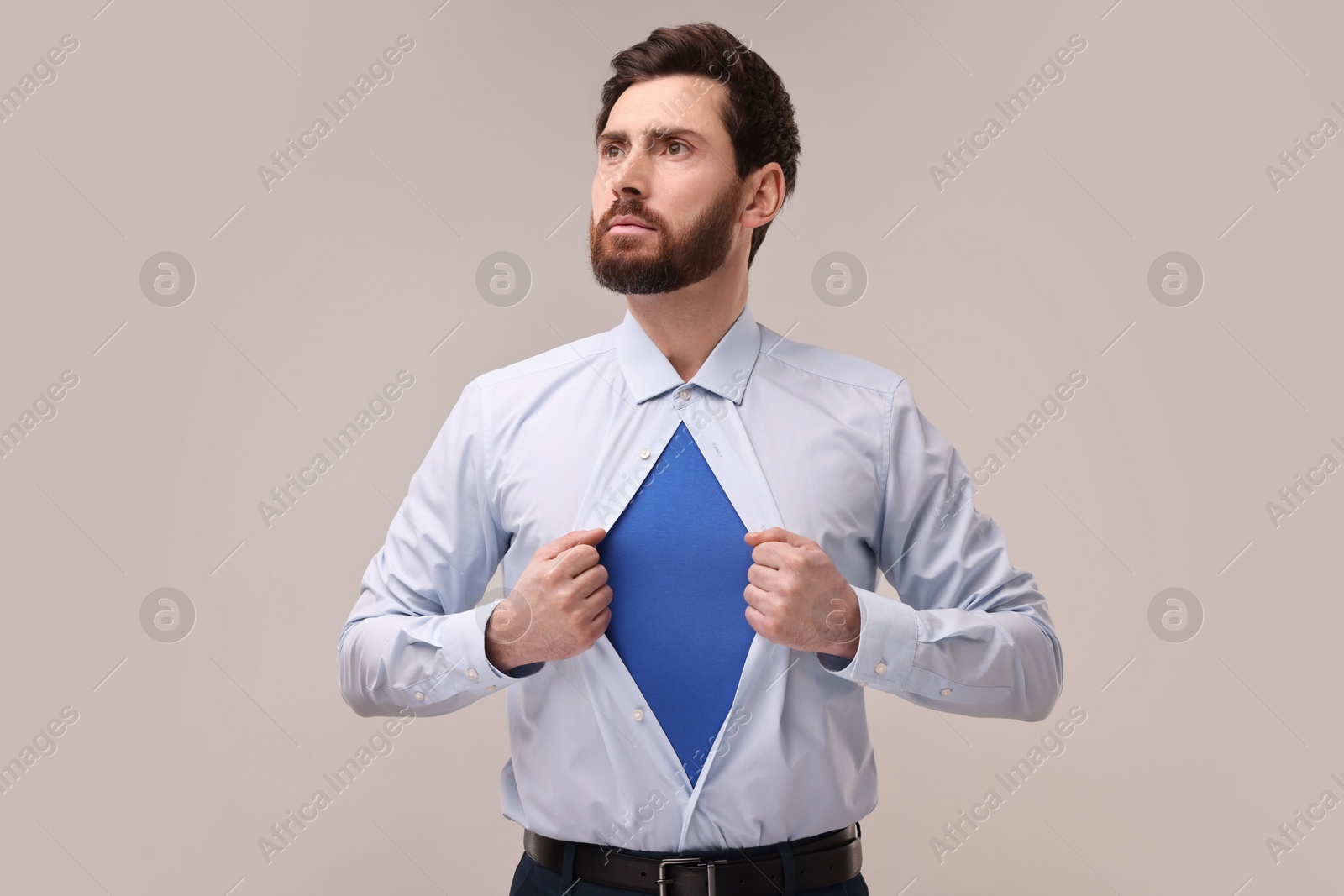 Photo of Confident businessman wearing superhero costume under suit on beige background