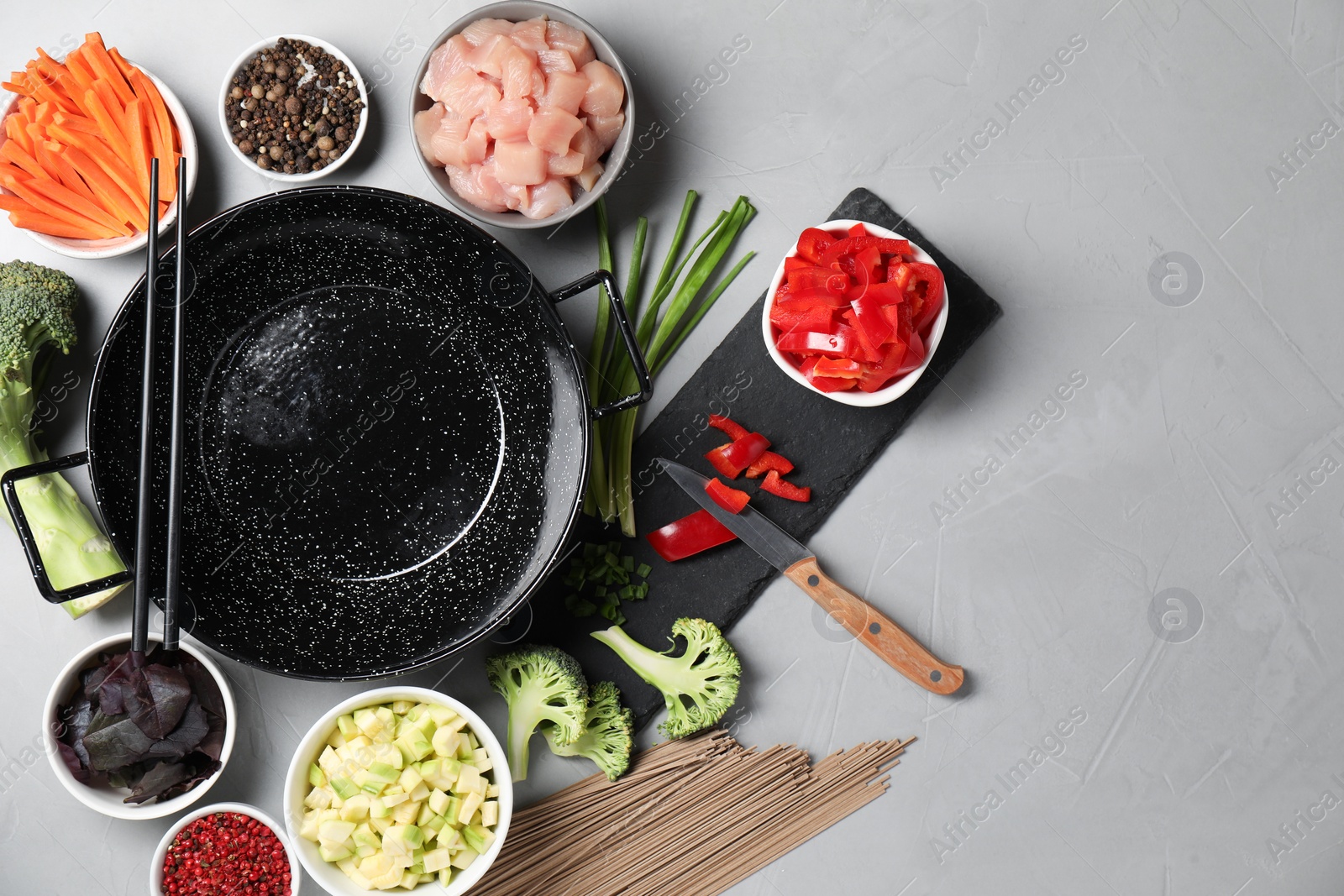 Photo of Wok pan, noodles, chicken and other products on light grey table, flat lay. Space for text