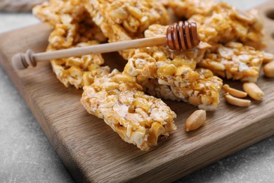 Photo of Delicious peanut kozinaki bars and honey dipper on wooden board, closeup