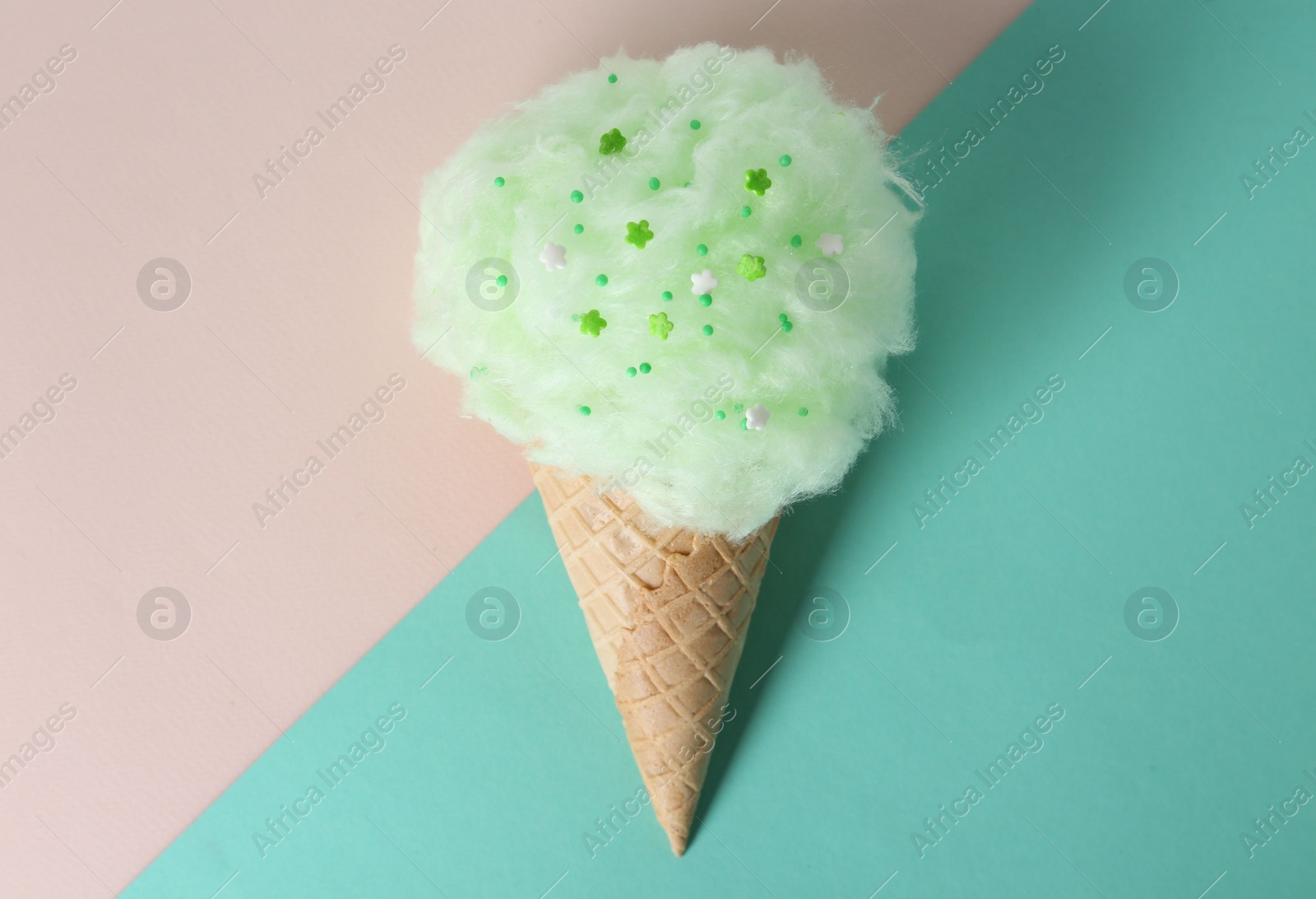 Photo of Sweet cotton candy in waffle cone on color background, top view