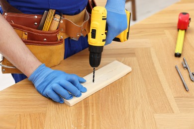 Young worker using electric drill at table in workshop, closeup