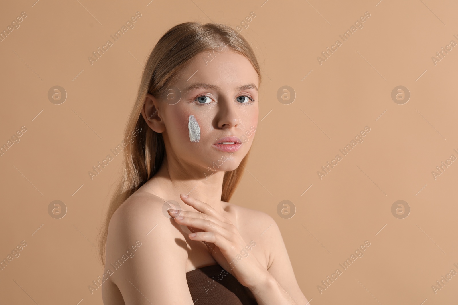 Photo of Beautiful young woman with sun protection cream on her face against beige background, space for text