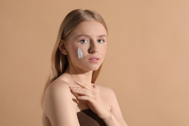 Beautiful young woman with sun protection cream on her face against beige background, space for text