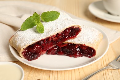 Photo of Delicious strudel with cherries, powdered sugar and mint on wooden table, closeup
