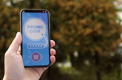 Photo of Man holding smartphone with activated promo code outdoors, closeup. Space for text