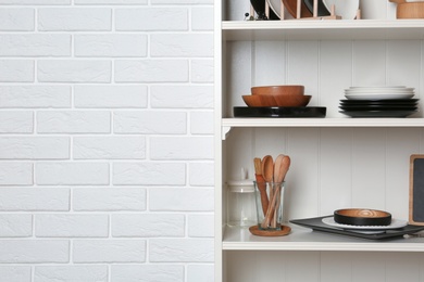 White shelving unit with set of dishware near brick wall. Space for text