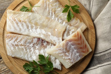 Photo of Fresh raw cod fillets and parsley on wooden table, top view