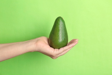 Woman holding ripe avocado on color background