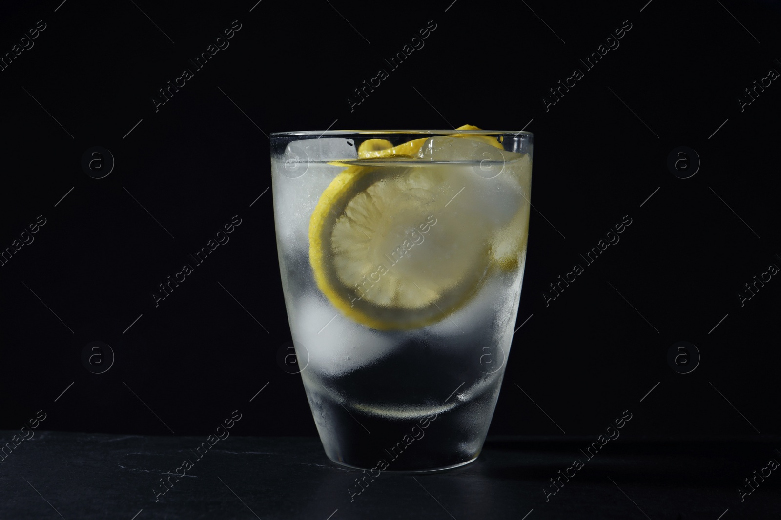 Photo of Shot of vodka with lemon and ice on black table