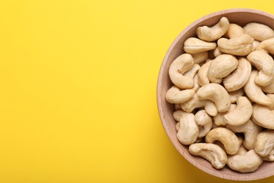 Tasty cashew nuts in bowl on yellow background, top view. Space for text