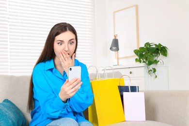 Special Promotion. Emotional young woman looking at smartphone on sofa indoors