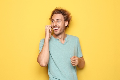 Young man talking on mobile phone on color background