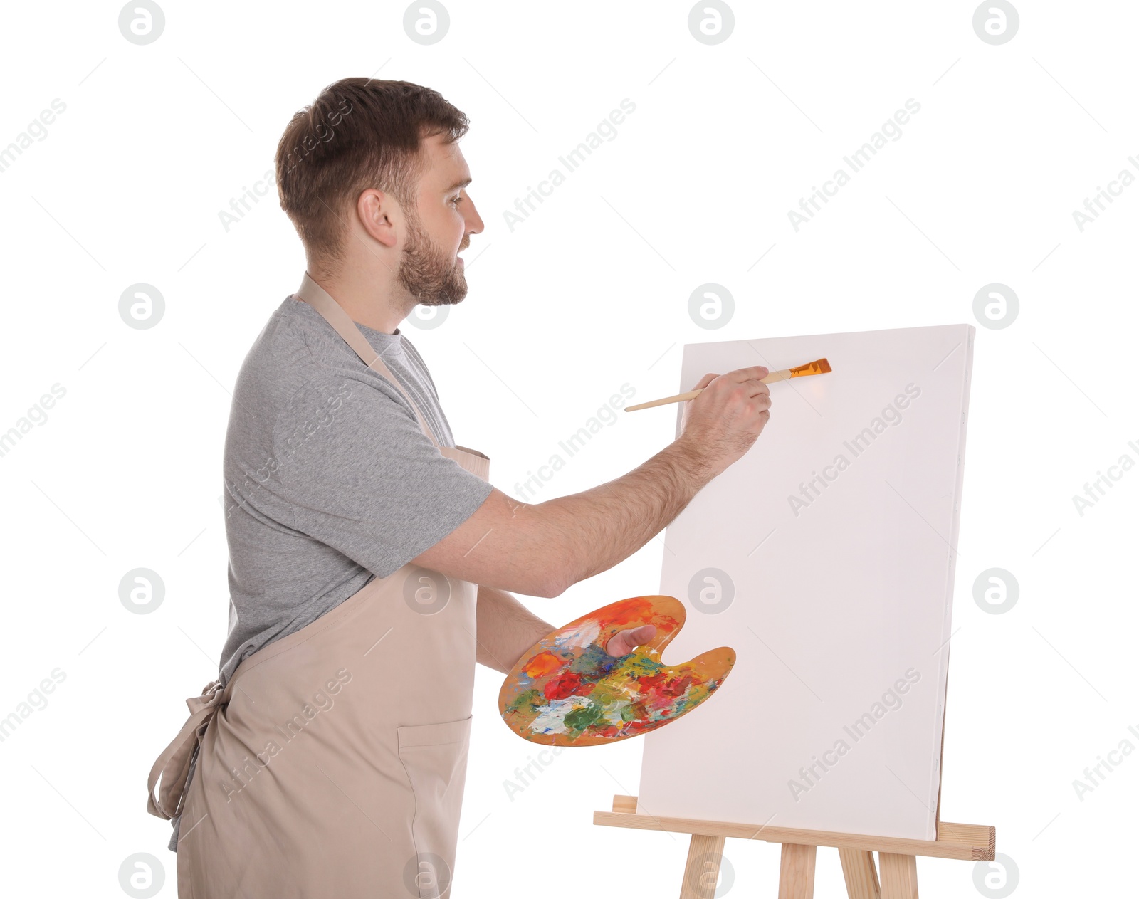 Photo of Man painting with brush on easel against white background. Young artist