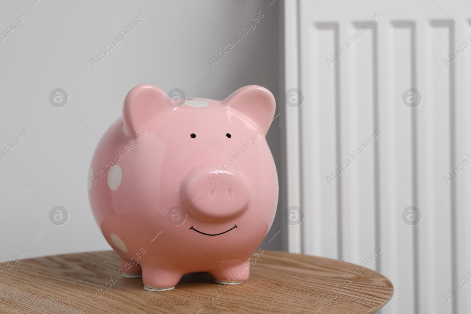 Photo of Piggy bank on wooden table near heating radiator, space for text