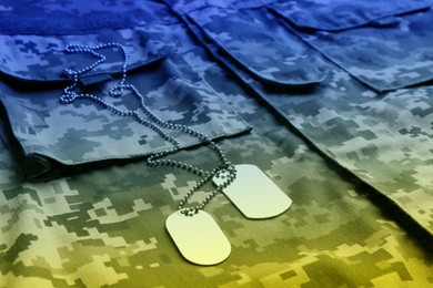 Image of Military ID tags with chain on camouflage uniform, toned in colors of Ukrainian flag