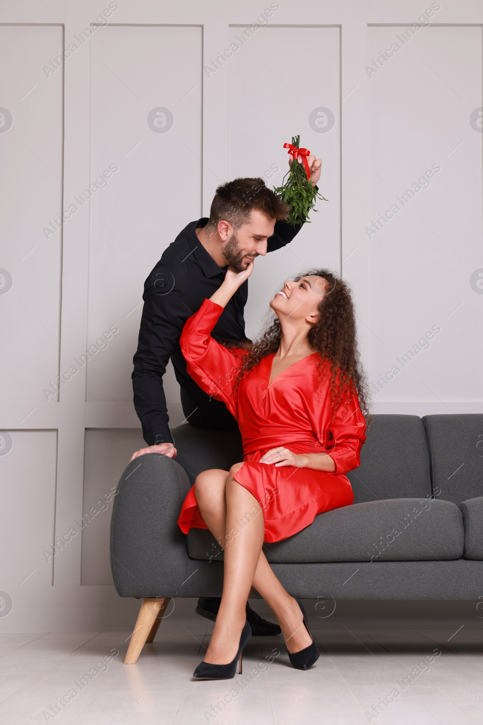 Photo of Lovely couple under mistletoe bunch near light grey wall indoors