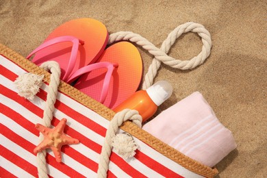 Photo of Stylish striped bag with beach accessories on sand, flat lay