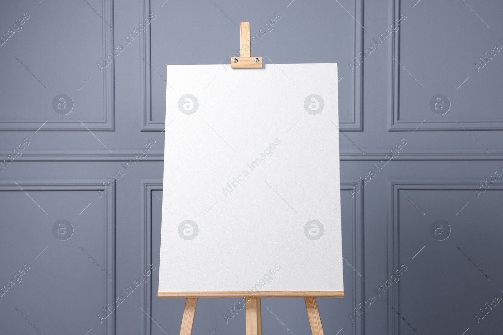 Photo of Wooden easel with blank canvas near grey wall indoors, closeup. Space for text