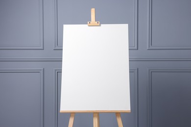 Photo of Wooden easel with blank canvas near grey wall indoors, closeup. Space for text