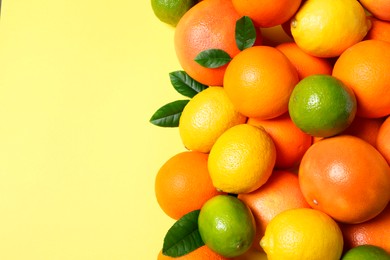 Photo of Different fresh citrus fruits and leaves on yellow background, flat lay. Space for text