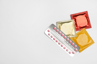 Condoms and birth control pills on light grey background, flat lay with space for text. Safe sex concept