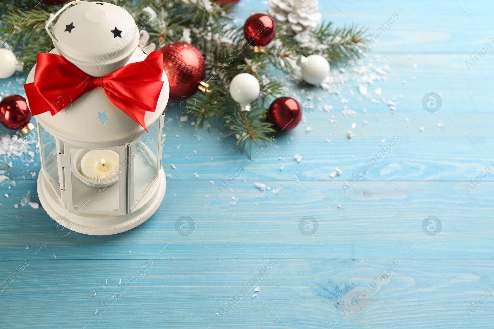 Photo of Christmas lantern with burning candle and festive decor on light blue wooden table. Space for text