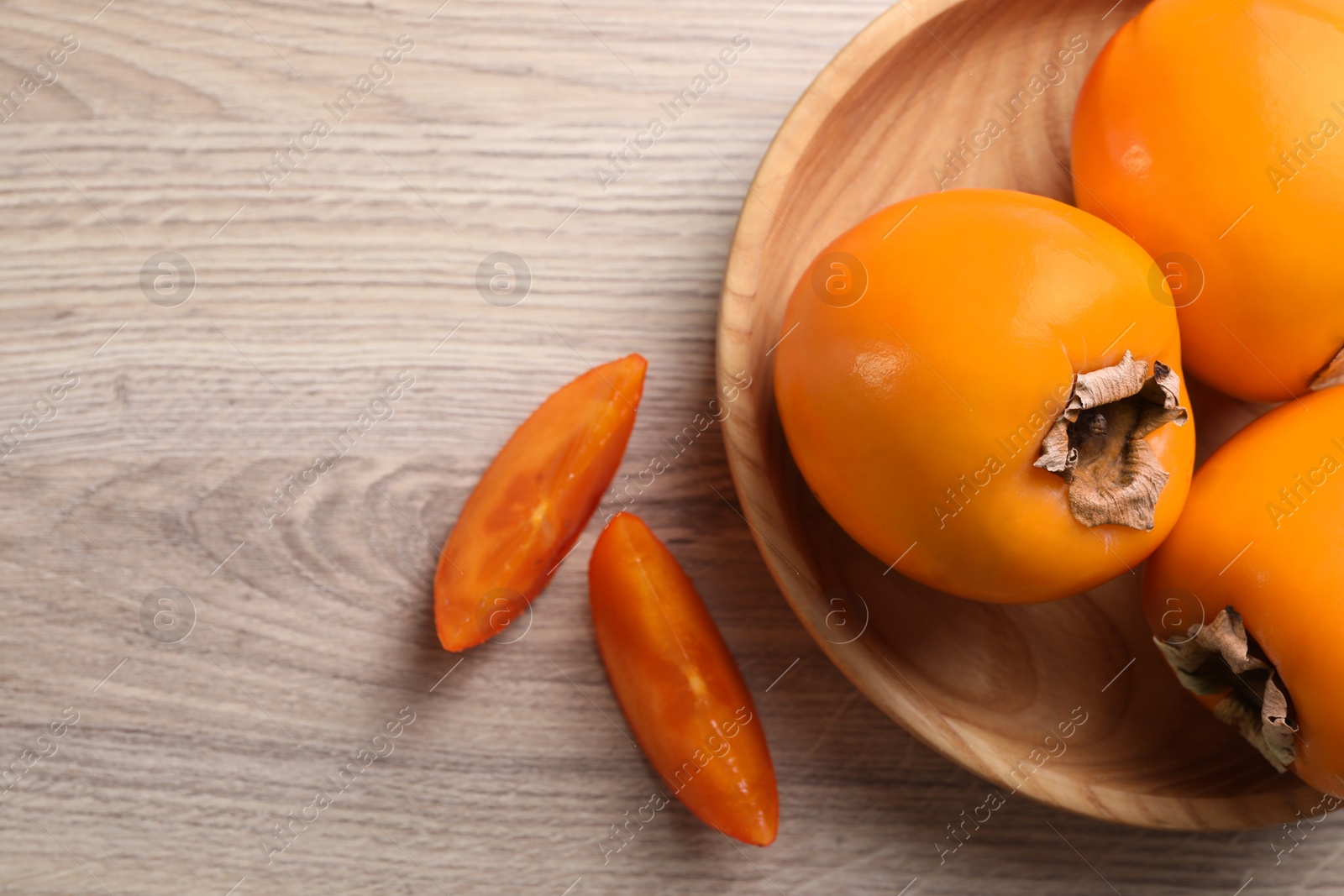 Photo of Delicious ripe persimmons on light wooden table, top view. Space for text