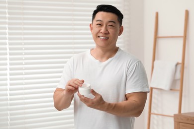 Handsome man with jar of body cream at home