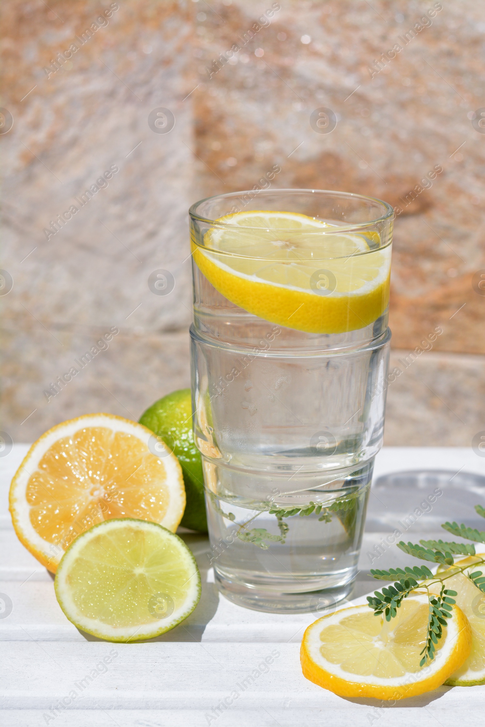 Photo of Delicious refreshing lemonade and pieces of citrus on white wooden table outdoors