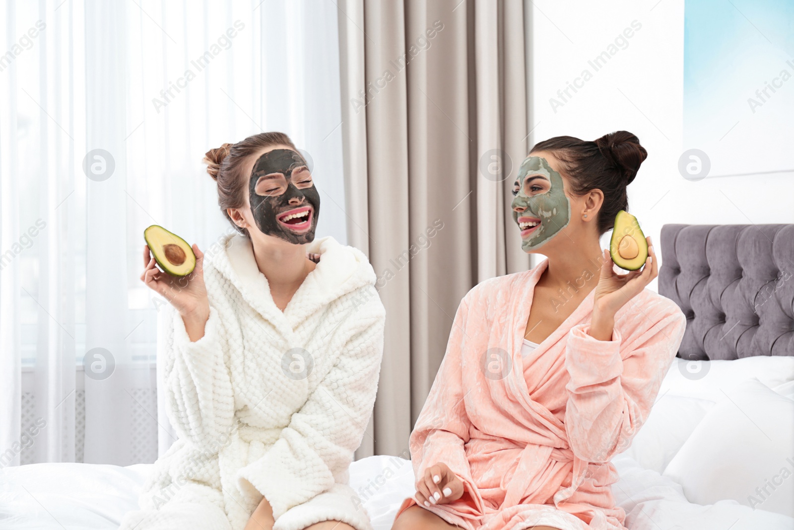 Photo of Young friends with facial masks having fun in bedroom at pamper party