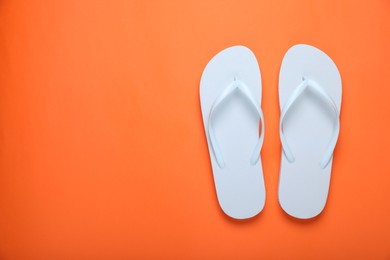 Stylish white flip flops on orange background, top view. Space for text