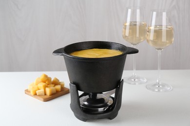 Photo of Fondue with tasty melted cheese and aromatic wine in glasses on white table