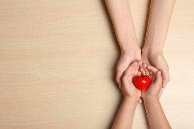 Woman and child holding heart on beige wooden background, top view with space for text. Donation concept