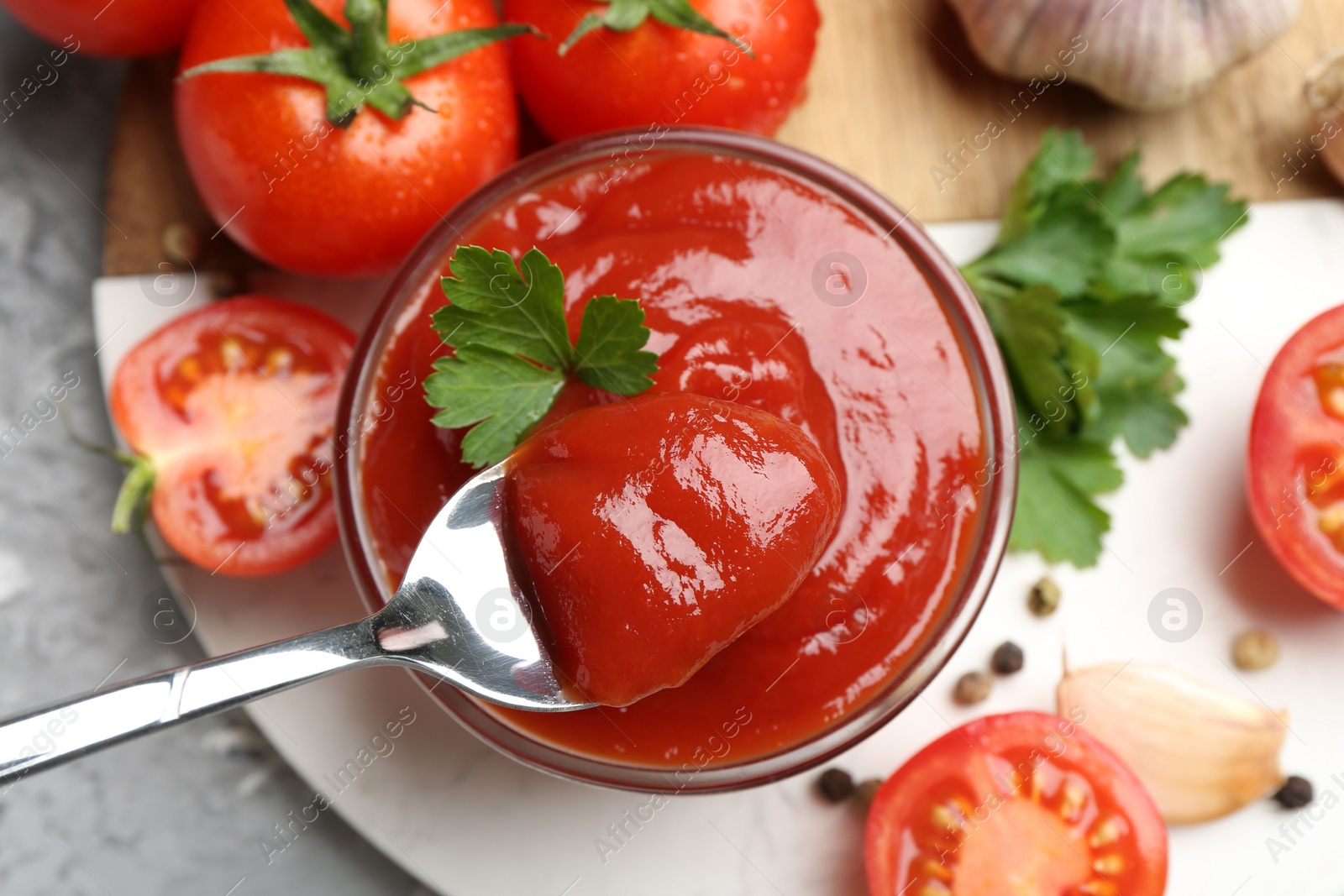 Photo of Taking delicious tomato ketchup with spoon from bowl at grey table, top view