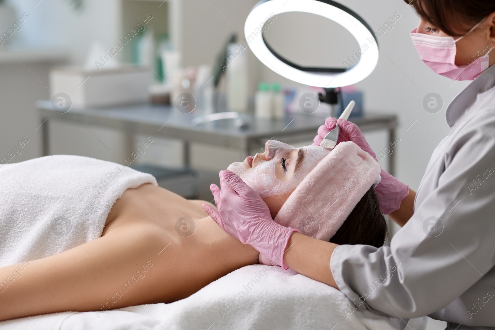 Photo of Cosmetologist applying mask on woman's face in clinic, closeup