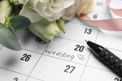 Photo of Calendar with date reminder about Wedding Day, pen and flowers, closeup