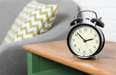 Analog alarm clock on side table in living room, space for text. Time of day