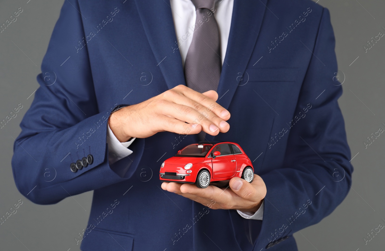 Photo of Insurance agent holding toy car on gray background, closeup