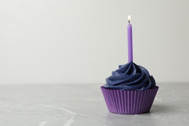 Photo of Delicious birthday cupcake with cream and burning candle on marble table. Space for text