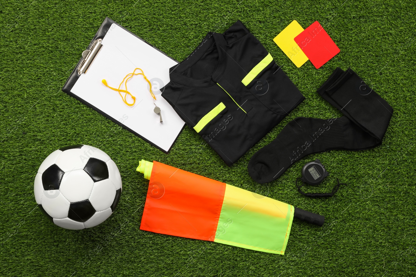 Photo of Uniform, soccer ball and other referee equipment on green grass, flat lay