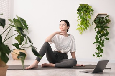 Photo of Beautiful girl sitting on yoga mat near laptop in studio