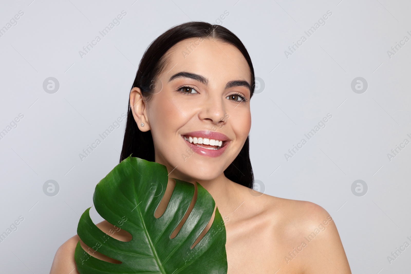 Photo of Woman holding leaf of monstera on light grey background. Spa treatment