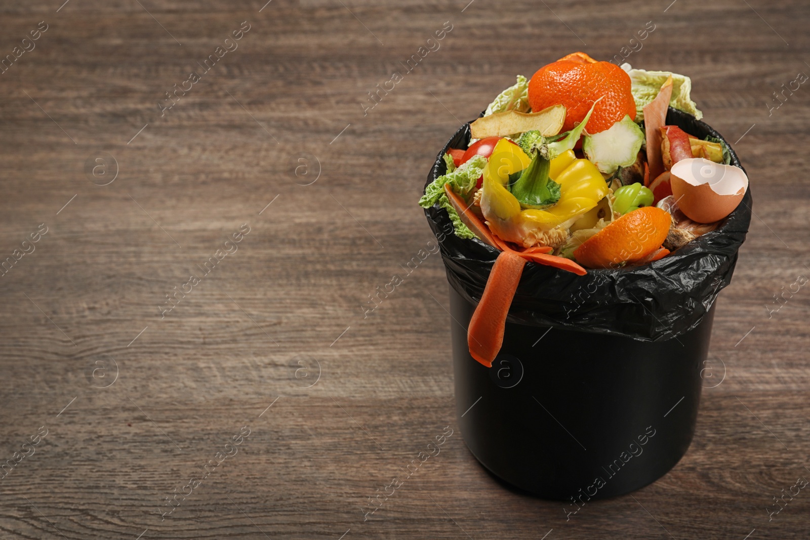 Photo of Trash bin with natural garbage on wooden background, space for text. Composting of organic waste