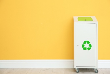 Photo of Trash bin with recycling symbol near color wall indoors. Space for text