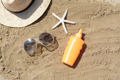 Blank bottle of sunscreen, starfish and beach accessories on sand, flat lay